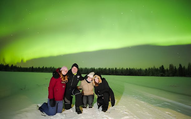 Guests on Northern Lights Discovery Tour under vibrant aurora borealis in snowy landscape.