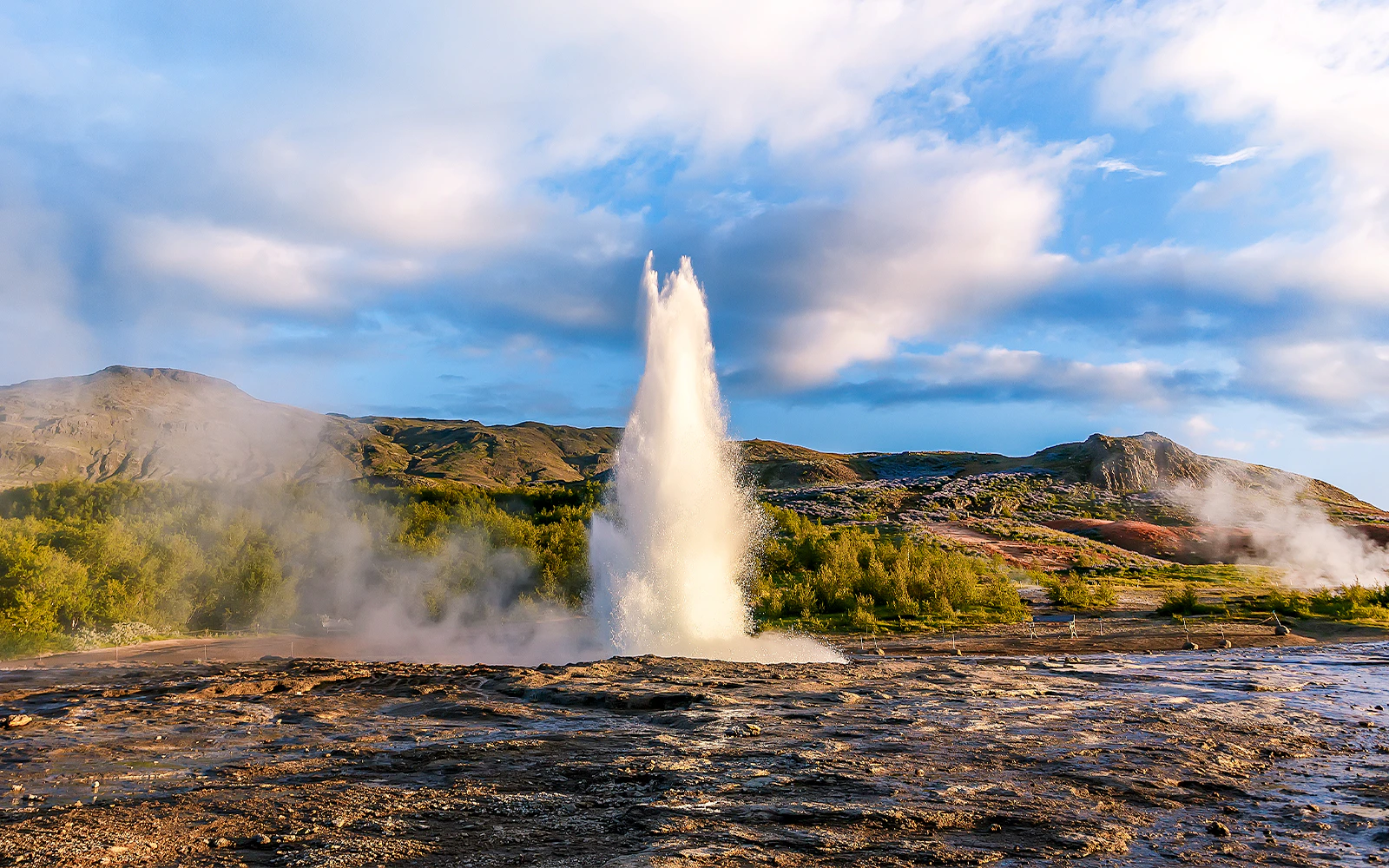 Geyser erupting in Icelandic hot springs landscape.