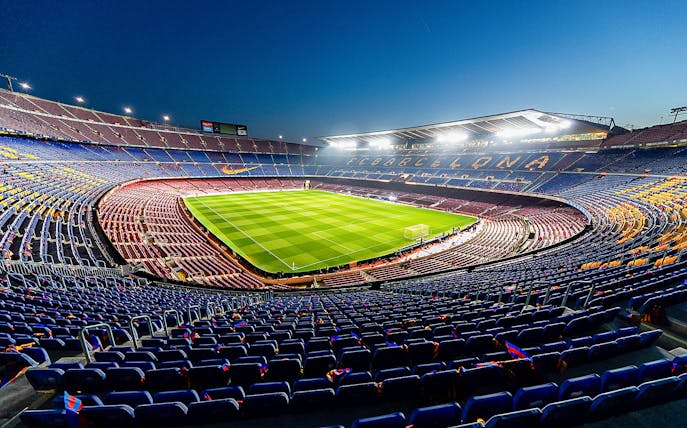 Camp Nou stadium in Barcelona, empty seats and illuminated field at dusk.