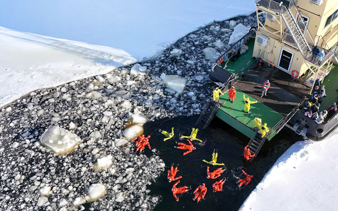 Participants in survival suits floating near an icebreaker on the Icebreaker Arktis Cruise, Kemi.