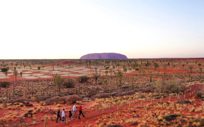 Uluru at sunrise with visitors walking through the Field of Light installation in Australia.