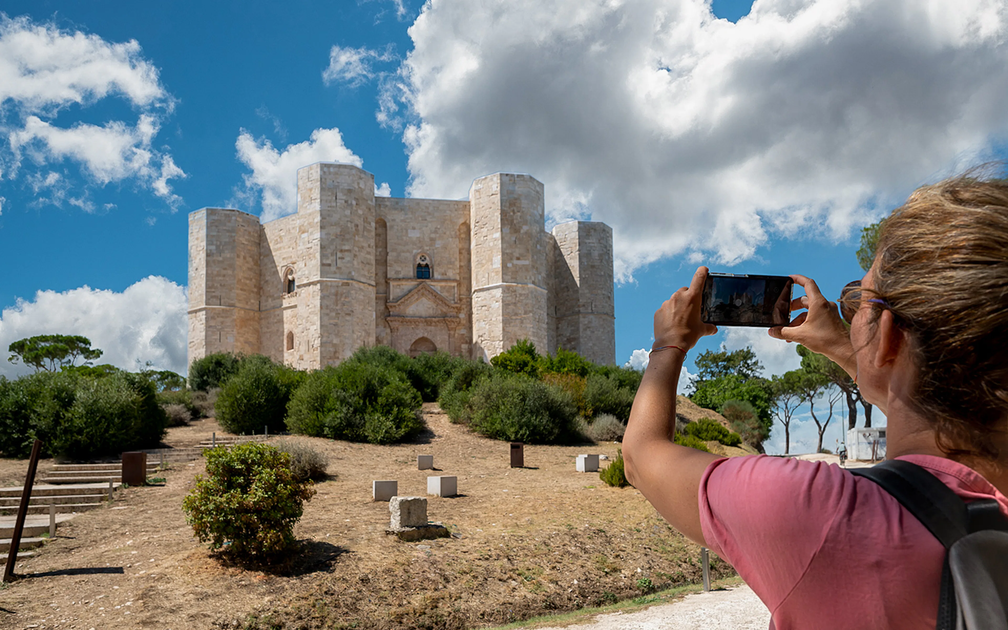 Visitor photographing Castel del Monte in Italy under a blue sky.