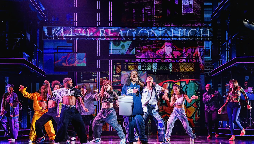 Performers dancing on stage in Hell's Kitchen show with vibrant graffiti backdrop.