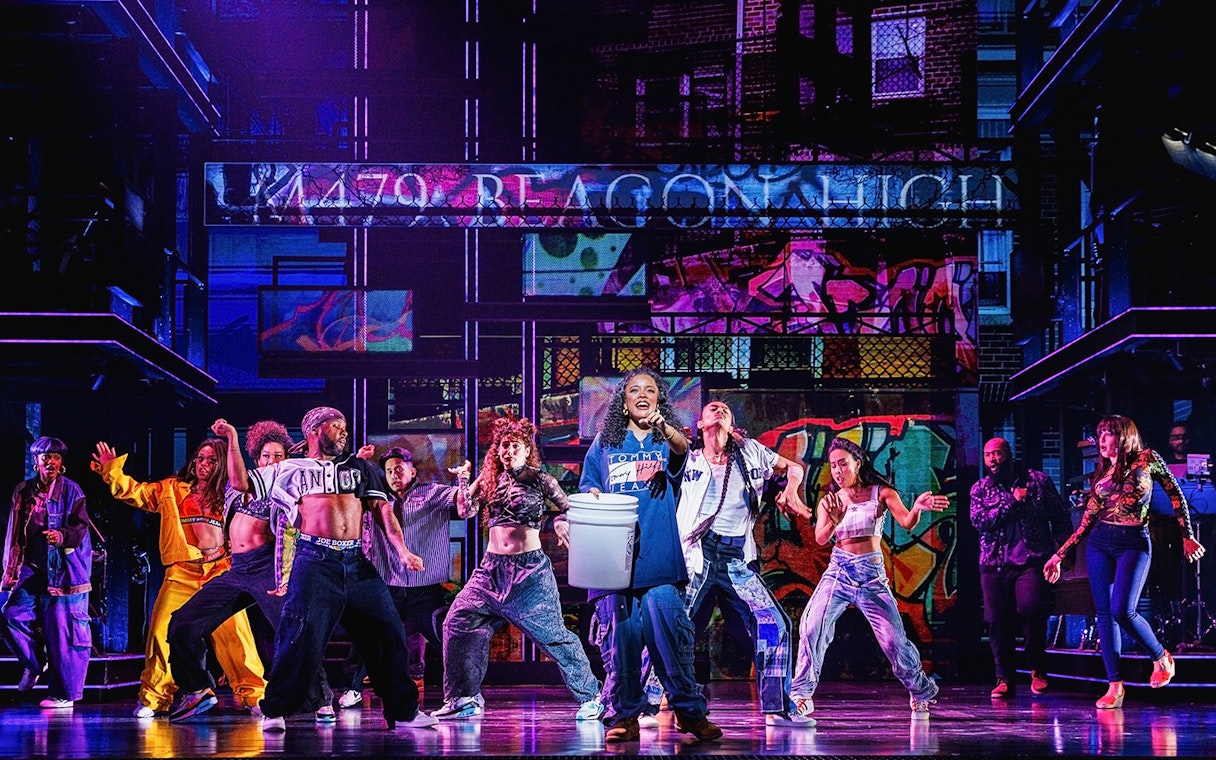 Performers dancing on stage in Hell's Kitchen show with vibrant graffiti backdrop.