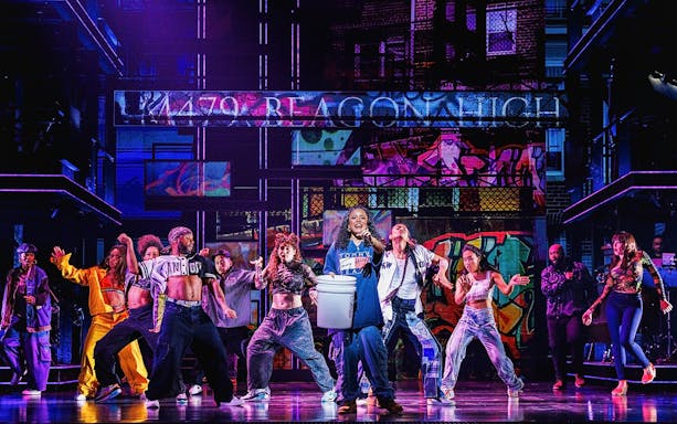 Performers dancing on stage in Hell's Kitchen show with vibrant graffiti backdrop.