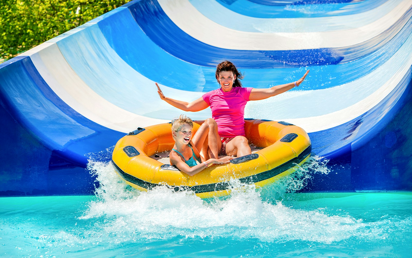 Mother and child on inflatable raft sliding down waterpark slide.