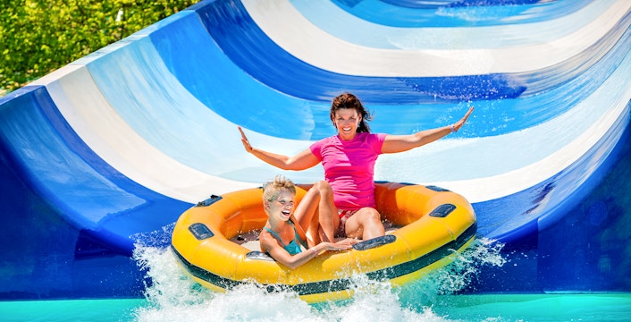 Mother and child on inflatable raft sliding down waterpark slide.