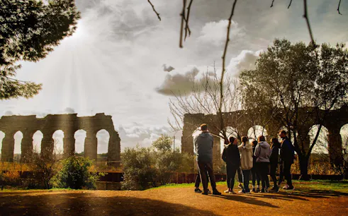 Group of people on Appian Way bike tour near Roman aqueducts in the countryside.
