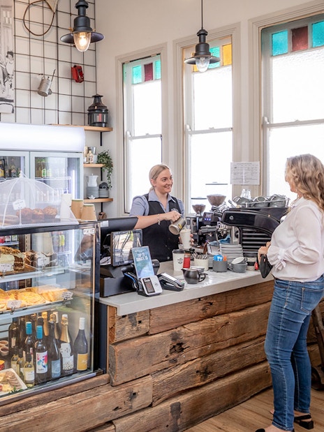 Cafe interior with pastries and drinks, barista serving a customer, part of Mary Valley Rattler Train Experience from Gympie.
