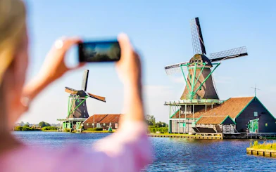 Windmills by the water in Volendam, Netherlands, with a person taking a photo.