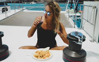 Woman enjoying a meal and drink on a boat during Lanzarote day trip to Papagayo Beaches.