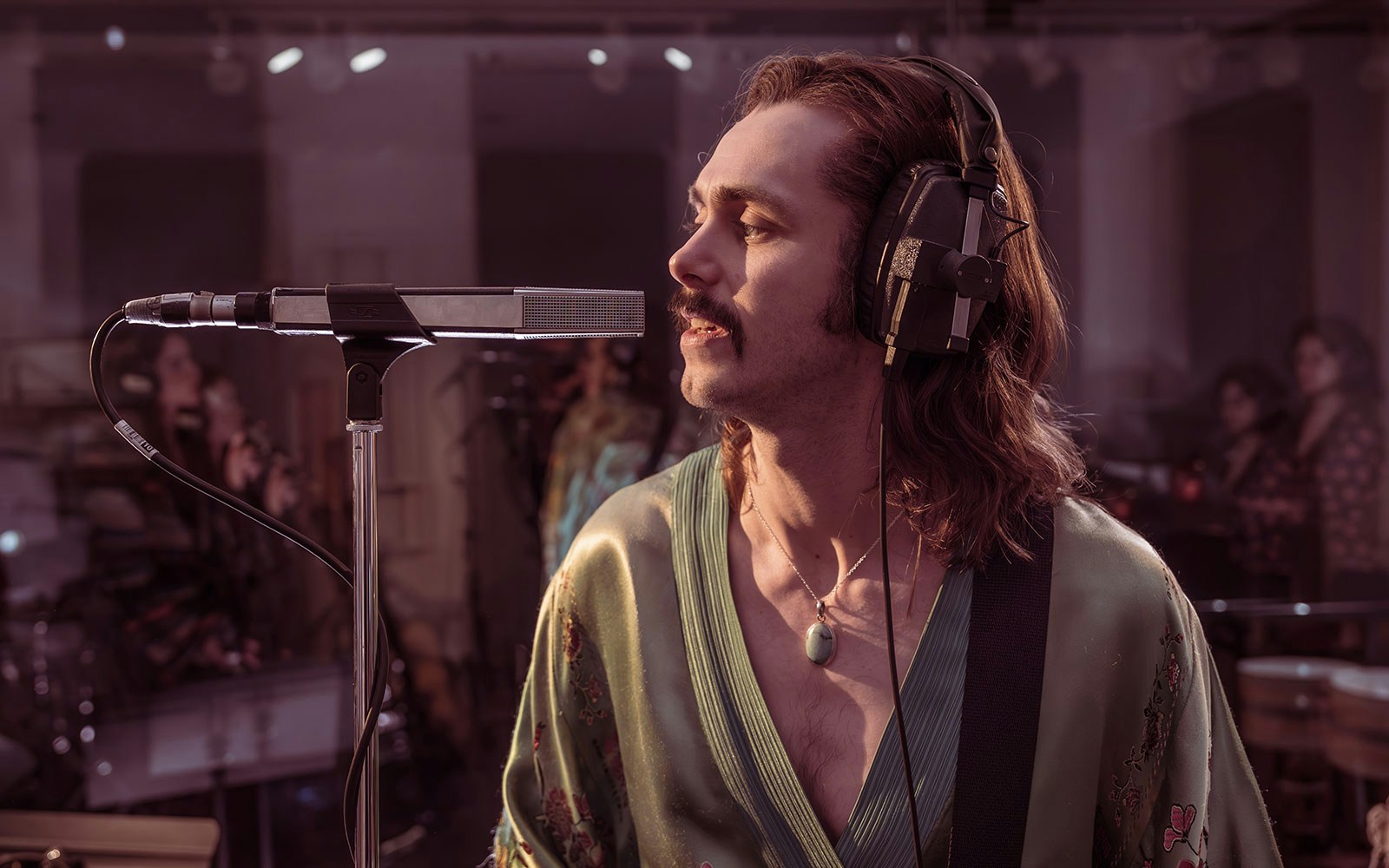 Musician recording vocals in a studio with headphones and microphone, related to Stereophonic.