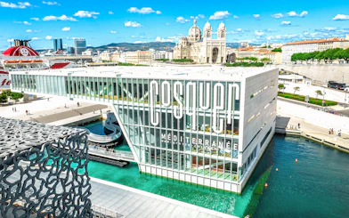 Cosquer Cave building in Marseille with waterfront view and cathedral in background.