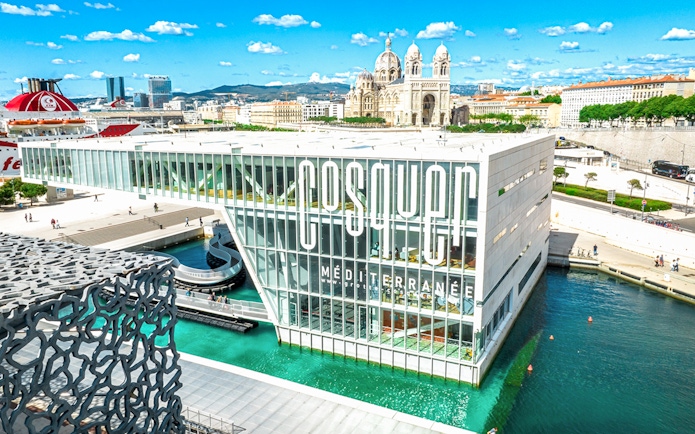 Cosquer Cave building in Marseille with waterfront view and cathedral in background.