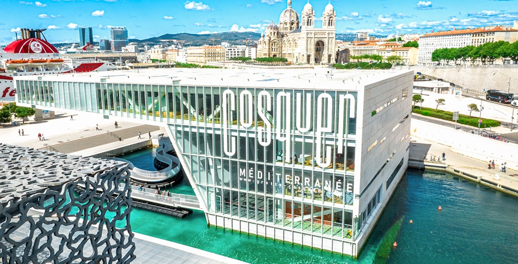 Cosquer Cave building in Marseille with waterfront view and cathedral in background.