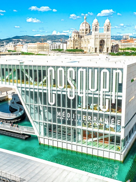 Cosquer Cave building in Marseille with waterfront view and cathedral in background.