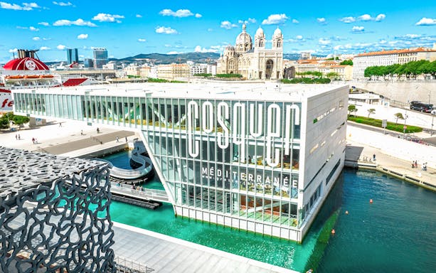 Cosquer Cave building in Marseille with waterfront view and cathedral in background.