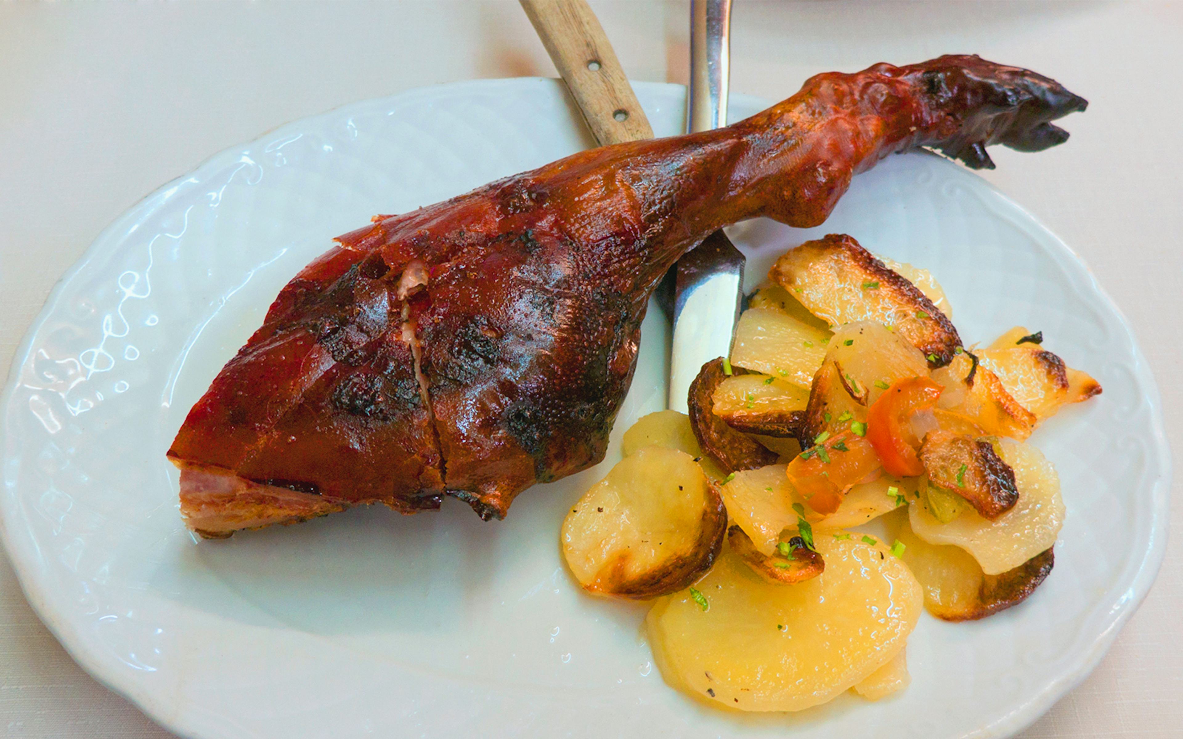 Roast suckling pig cochinillo with roasted potatoes on a white plate.