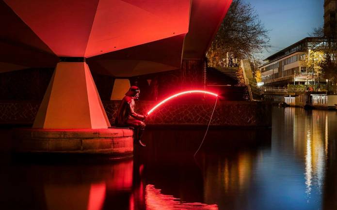 Person with glowing rod at Amsterdam Light Festival canal installation.