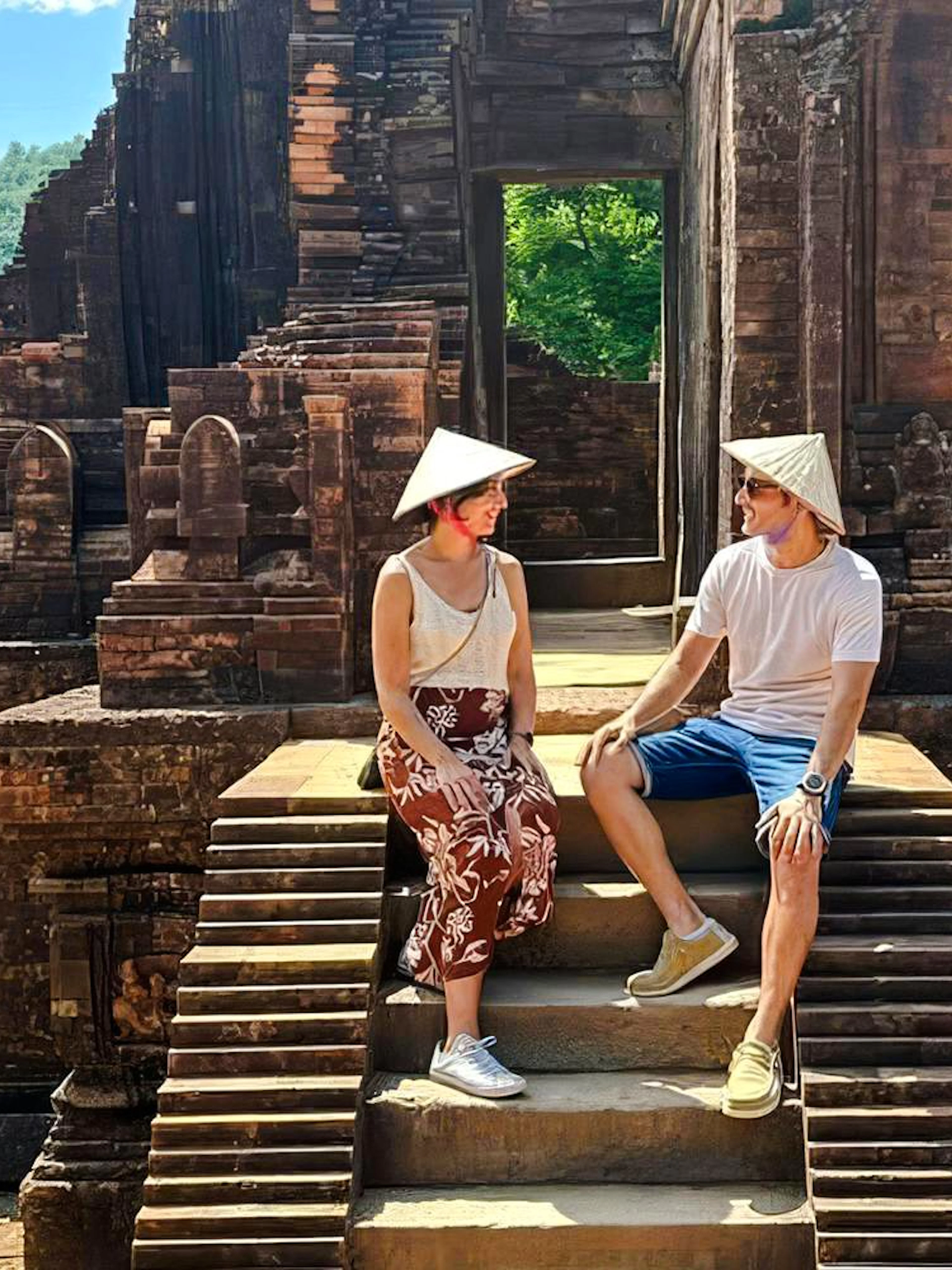Visitors sitting on steps at Mỹ Sơn Sanctuary, Vietnam, with ancient temple ruins in the background.