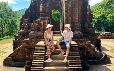 Visitors sitting on steps at Mỹ Sơn Sanctuary, Vietnam, with ancient temple ruins in the background.