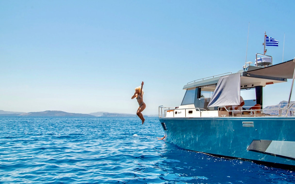 Catamaran cruise in Santorini with person jumping into the Aegean Sea.