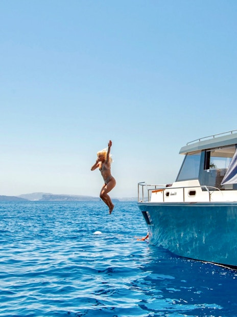 Catamaran cruise in Santorini with person jumping into the Aegean Sea.