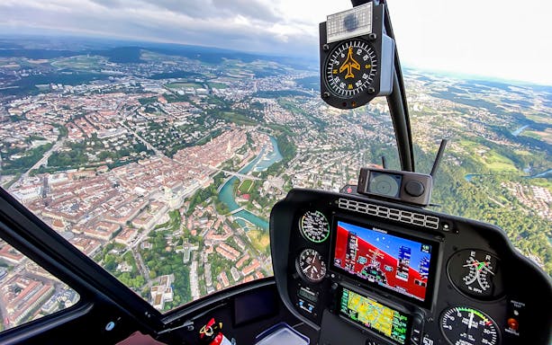 Aerial view from helicopter cockpit over Bern, Switzerland, showcasing cityscape and Aare River.