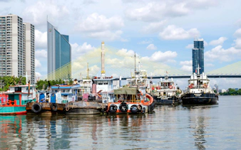 Boats docked on the Chao Phraya River with Bangkok skyline and bridge in the background.