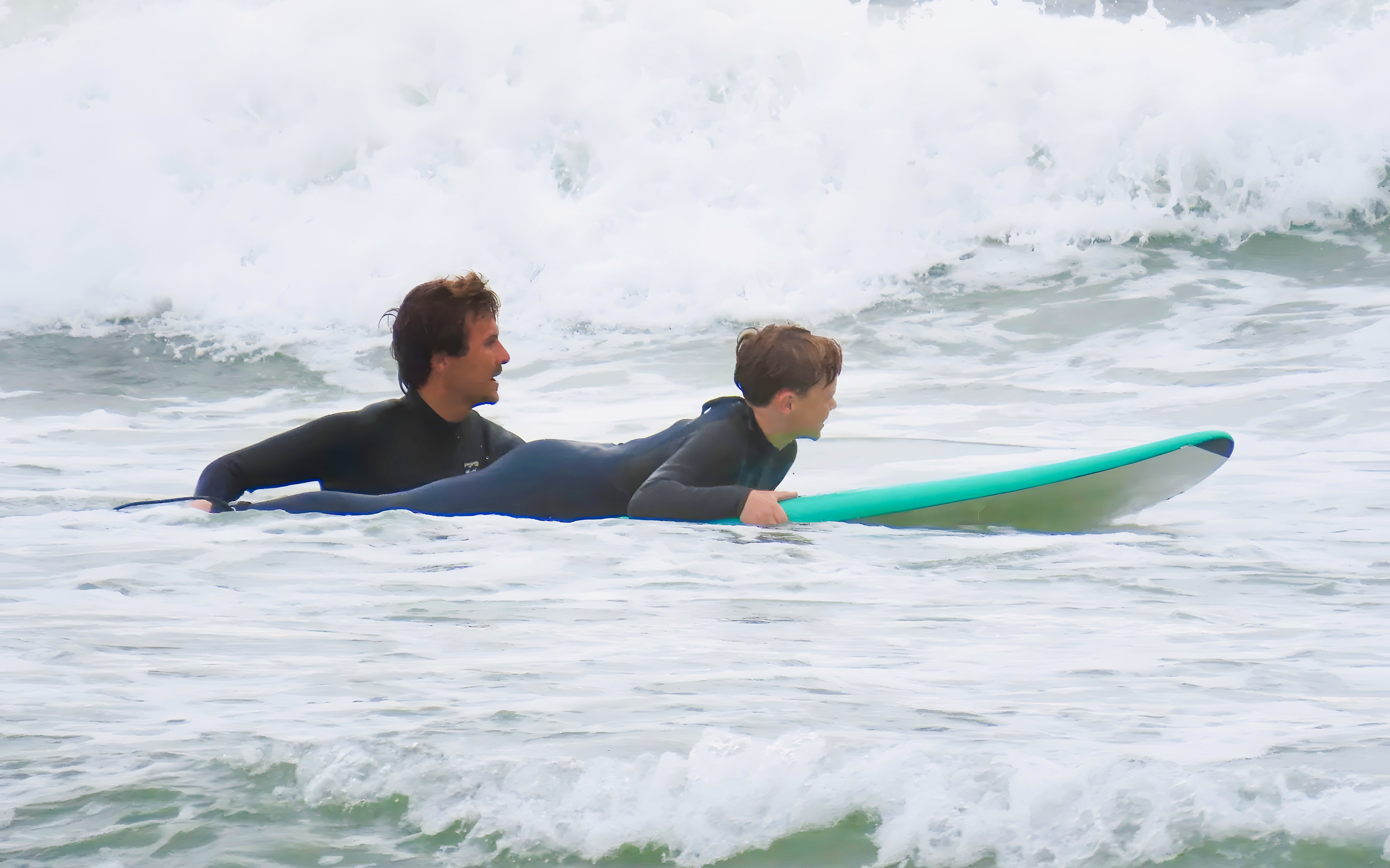 Instructor guiding child on surfboard in Lisbon surf class.
