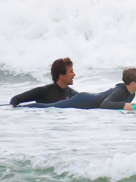 Instructor guiding child on surfboard in Lisbon surf class.
