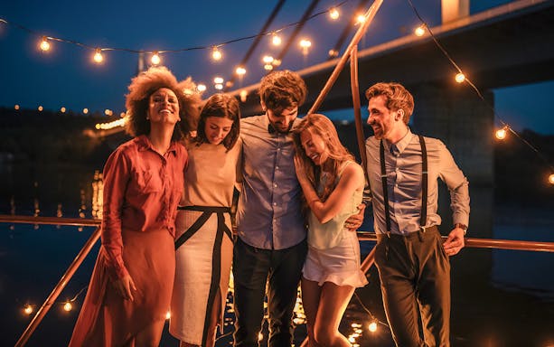 Friends enjoying an evening cruise under string lights by a bridge.