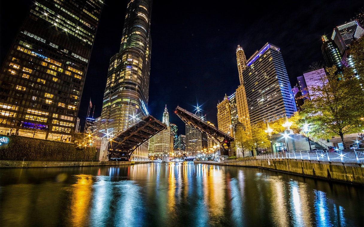 Chicago River at night with open lift bridge and illuminated skyline during architecture cruise.