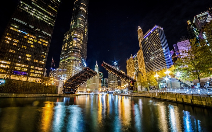 Chicago River at night with open lift bridge and illuminated skyline during architecture cruise.