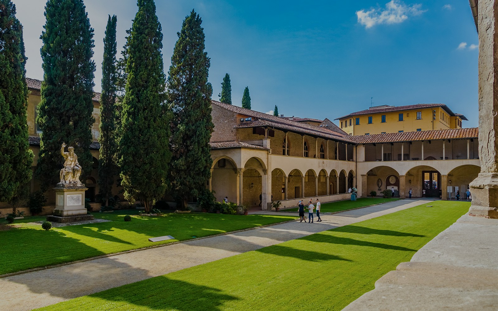 Cloisters of Santa Croce Basilica Complex with statue and visitors in Florence, Italy.
