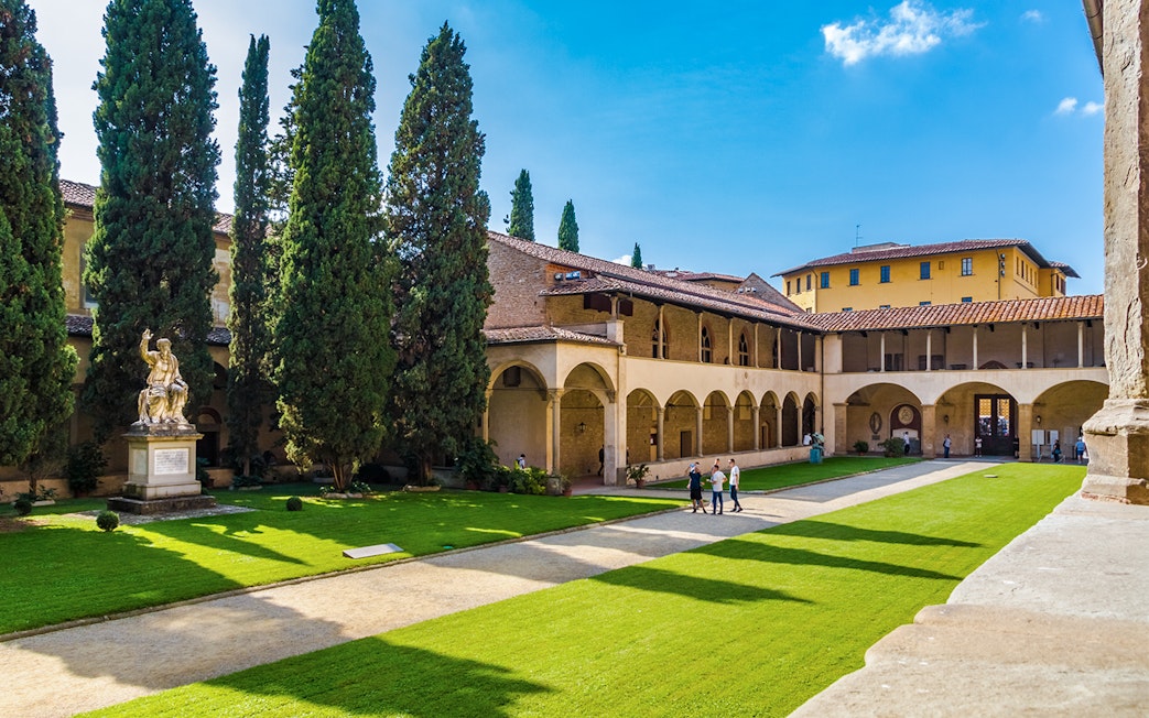 Cloisters of Santa Croce Basilica Complex with statue and visitors in Florence, Italy.