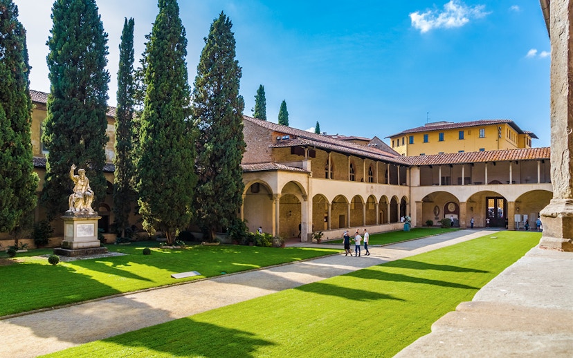 Cloisters of Santa Croce Basilica Complex with statue and visitors in Florence, Italy.