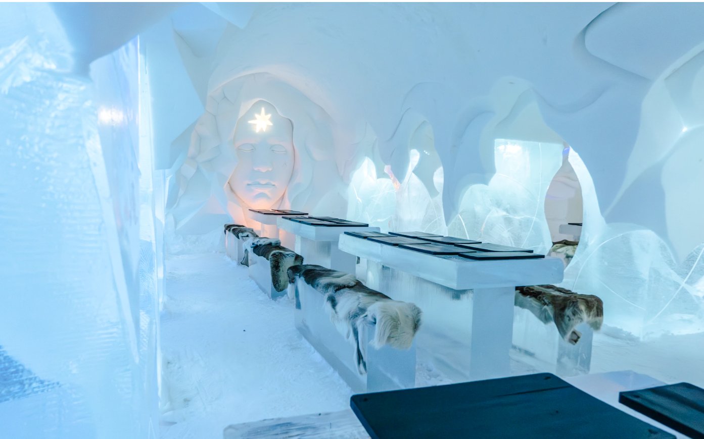 Inside view of Arctic SnowHotel dining area with ice tables and carved ice wall.