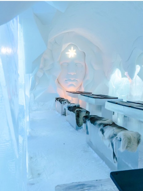 Inside view of Arctic SnowHotel dining area with ice tables and carved ice wall.