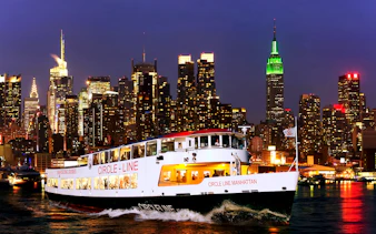 Tourists on Circle Line cruise with New York skyline illuminated at dusk.