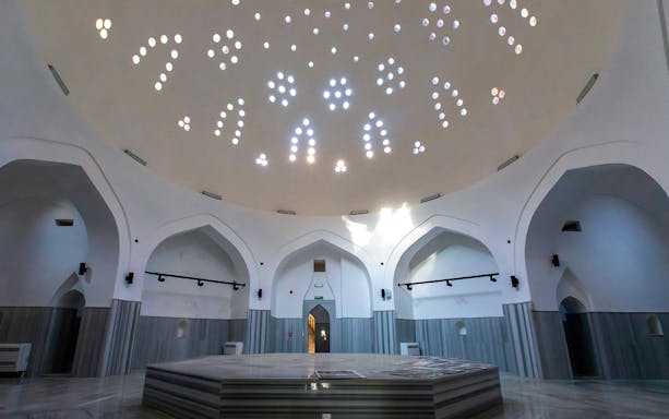 Domed interior of a historical Turkish bath in Istanbul with marble platform.