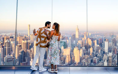 Couple enjoying sunset view from The Edge, New York City skyline in background.