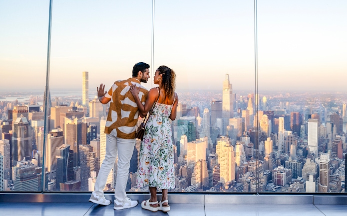 Couple enjoying sunset view from The Edge, New York City skyline in background.