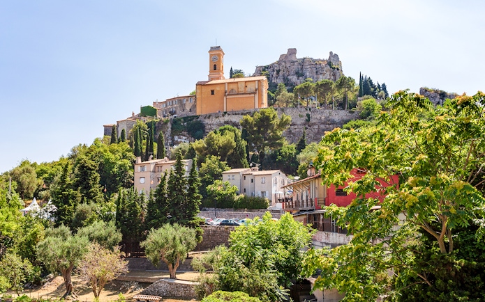 Eglise Notre Dame de L'Assomption on a hill in Eze, surrounded by trees and historic buildings.