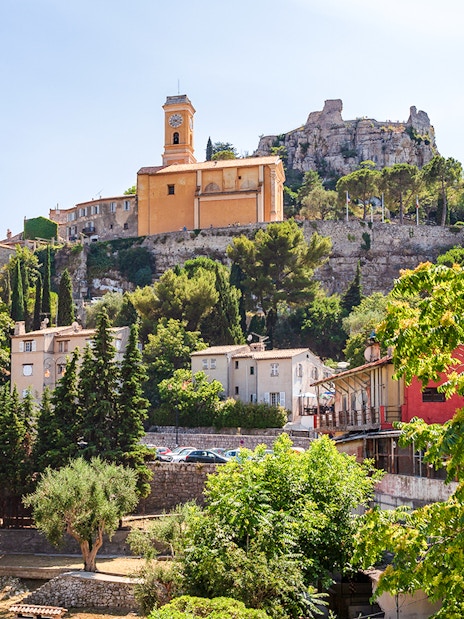 Eglise Notre Dame de L'Assomption on a hill in Eze, surrounded by trees and historic buildings.