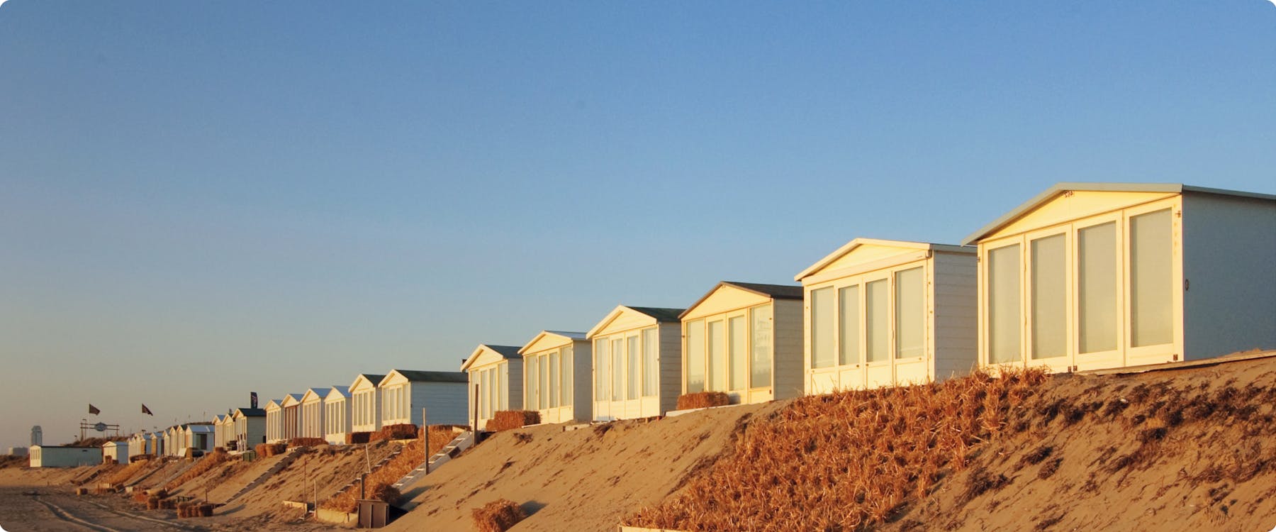 Beachfront cabins on sandy dunes in Zandvoort at sunset.