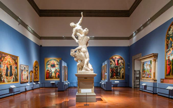 Statue and paintings in Academia Gallery, Florence, with skip-the-line ticket option.
