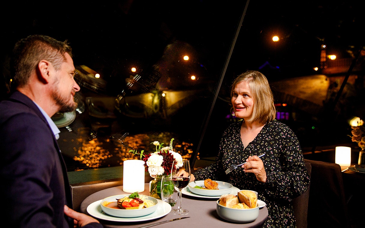 Couple dining on Seine River cruise with Paris lights in background.