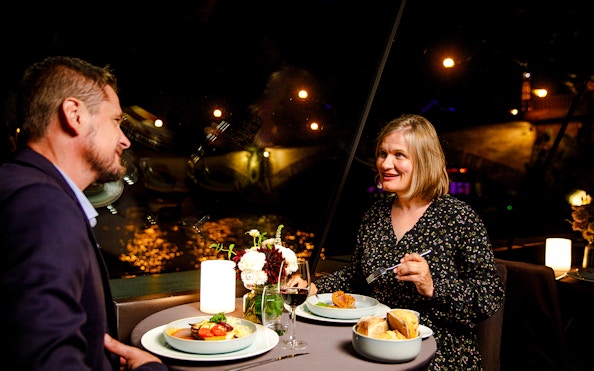 Couple dining on Seine River cruise with Paris lights in background.