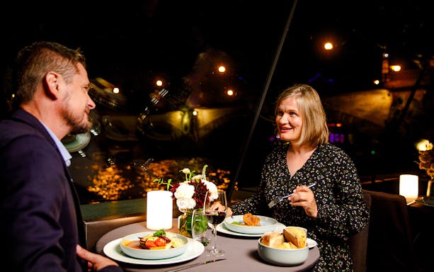 Couple dining on Seine River cruise with Paris lights in background.